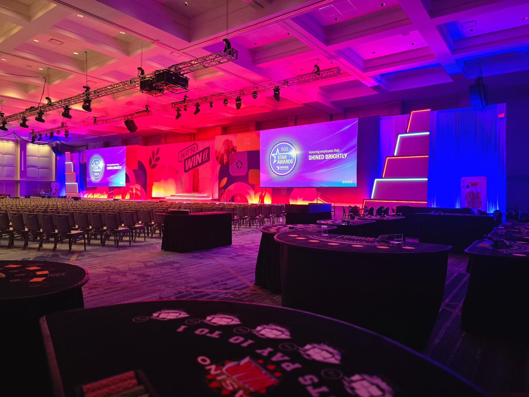 Casino tables arranged beside a brightly lit awards stage for a large fundraising event