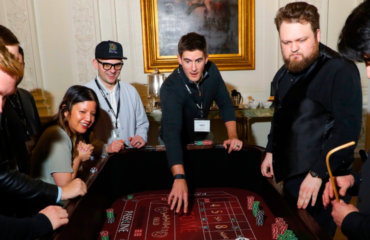 group of 21 fun party guests smiling and playing around a craps table at a corporate event