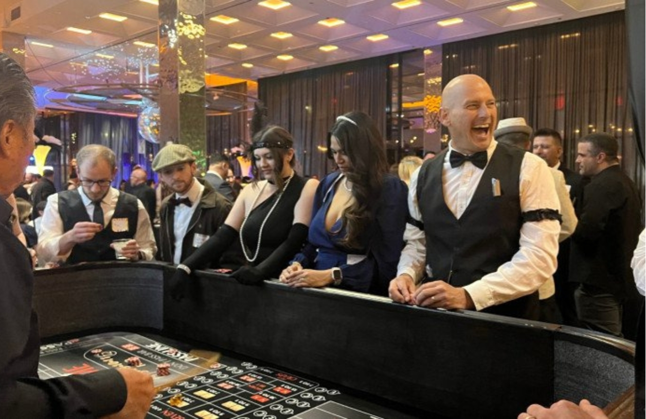 guests laugh and smile around a craps table at a themed casino night