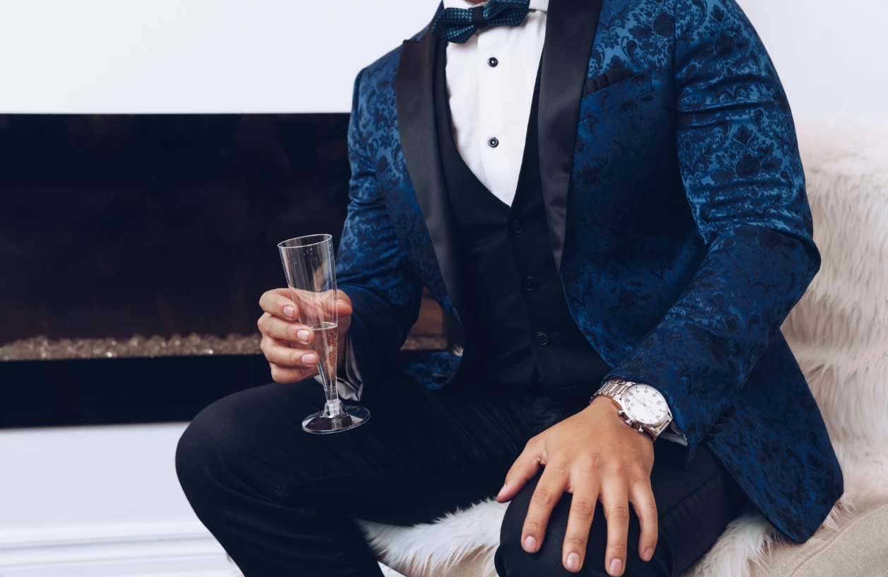 a man dressed in a midnight blue velvet blazer and elegant watch holding a glass of champagne at a casino themed party