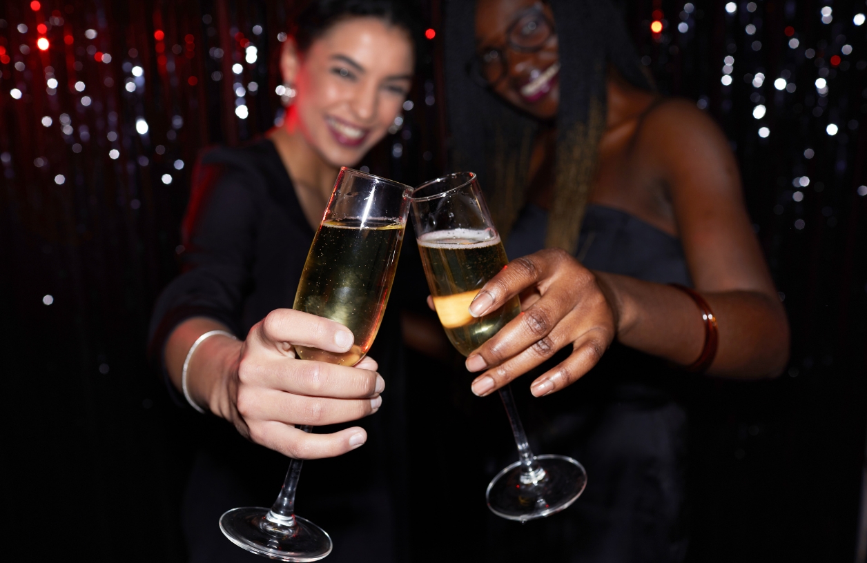 two women smile and share a toast with champagne glasses at a casino themed party