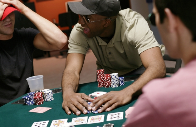 an excited man collects his winnings at a poker table while his friends stare in disbelief