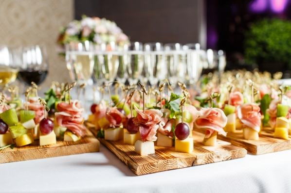 casino party catering display with skewers of prosciutto, cheese, grapes, and champagne flutes on a white table—perfect finger foods for upscale casino night events